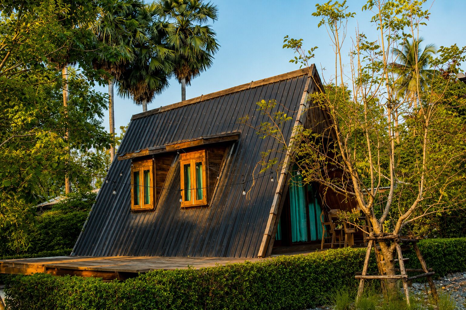 Een huis met een schuin dak, twee ramen met houten kaders en een houten terras.