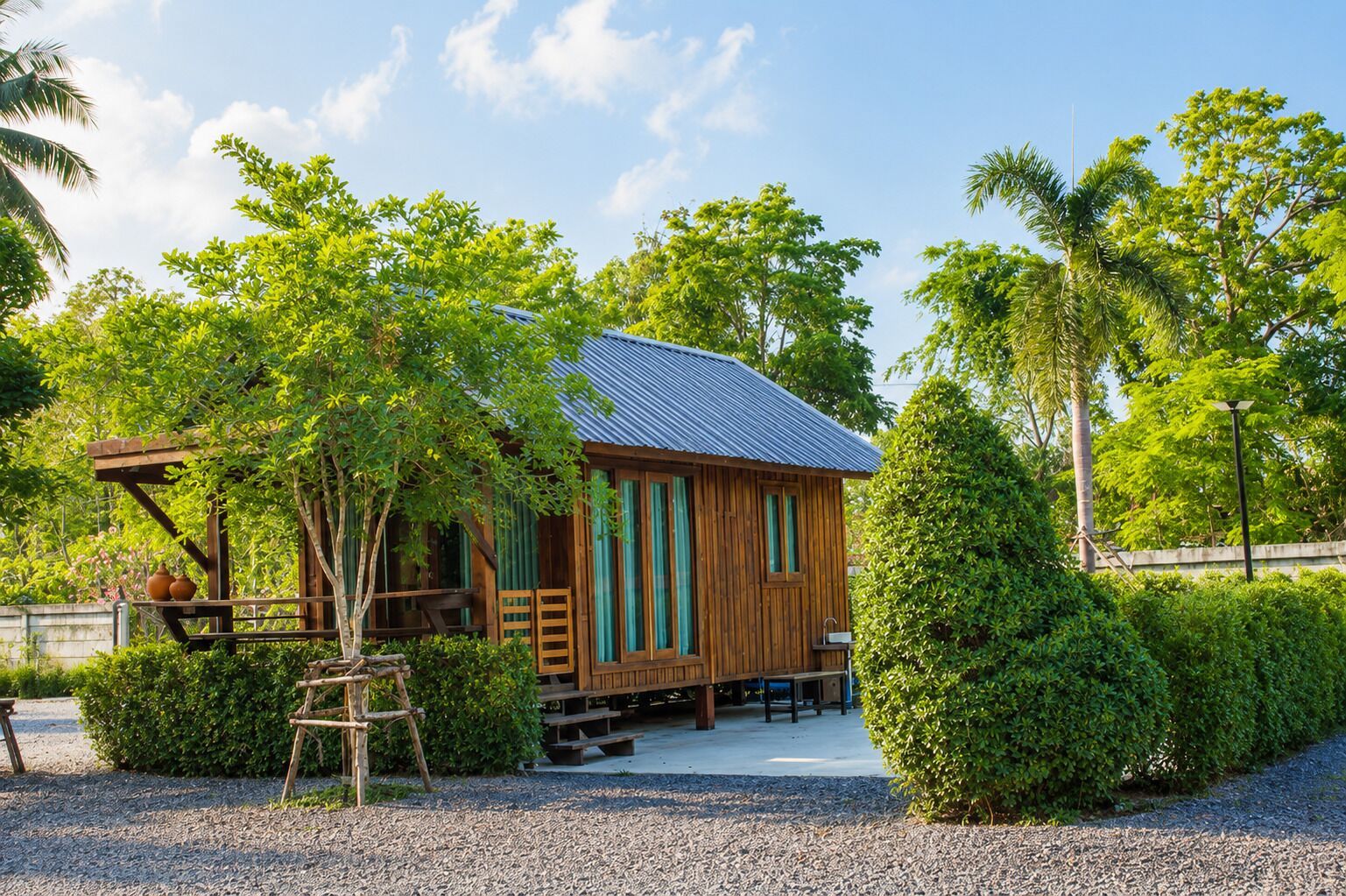 A wooden cabin with a metal roof, surrounded by lush greenery and a gravel path.