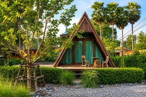 A triangular wooden structure with a green curtain, surrounded by lush greenery and palm trees. - Punnattha House by Peema Villa (U Thong)
