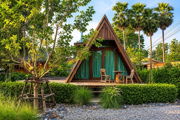 A triangular wooden structure with a green curtain, surrounded by lush greenery and palm trees. - Punnattha House by Peema Villa (U Thong)