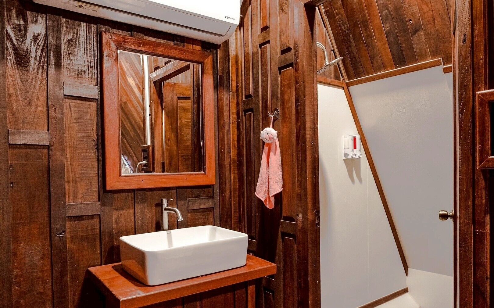 A bathroom with a wooden vanity, a white sink, a mirror, and a towel hanging on the wall.