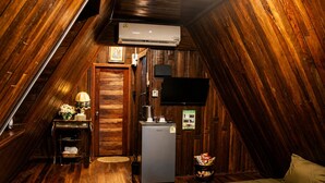 An attic room with wooden walls, a ceiling fan, a flat-screen TV, a refrigerator, and a bed. - Punnattha House by Peema Villa (U Thong)