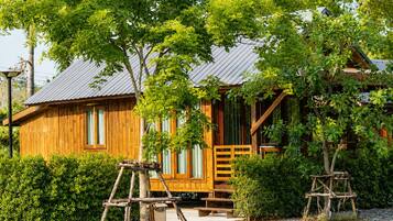 A wooden cabin with a metal roof, surrounded by lush greenery and a gravel path.