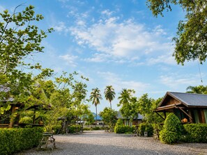 A rural setting with a gravel path, wooden structures, and lush greenery. - Punnattha House by Peema Villa (U Thong)