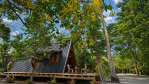 A rustic cabin with a sloped roof, wooden deck, and a small table and chair set outside. - Punnattha House by Peema Villa (U Thong)
