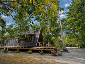 A rustic cabin with a sloped roof, wooden deck, and a small table and chair set outside. - Punnattha House by Peema Villa (U Thong)