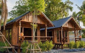A rustic wooden cabin with a porch, surrounded by greenery and trees. - Punnattha House by Peema Villa (U Thong)