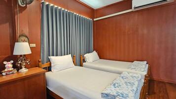 Una habitación de hotel con dos camas, una mesita de noche con lámpara, un ventilador y un equipo de aire acondicionado.