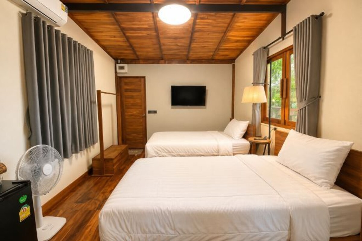 A room with two beds, a TV, a fan, and a window with curtains.