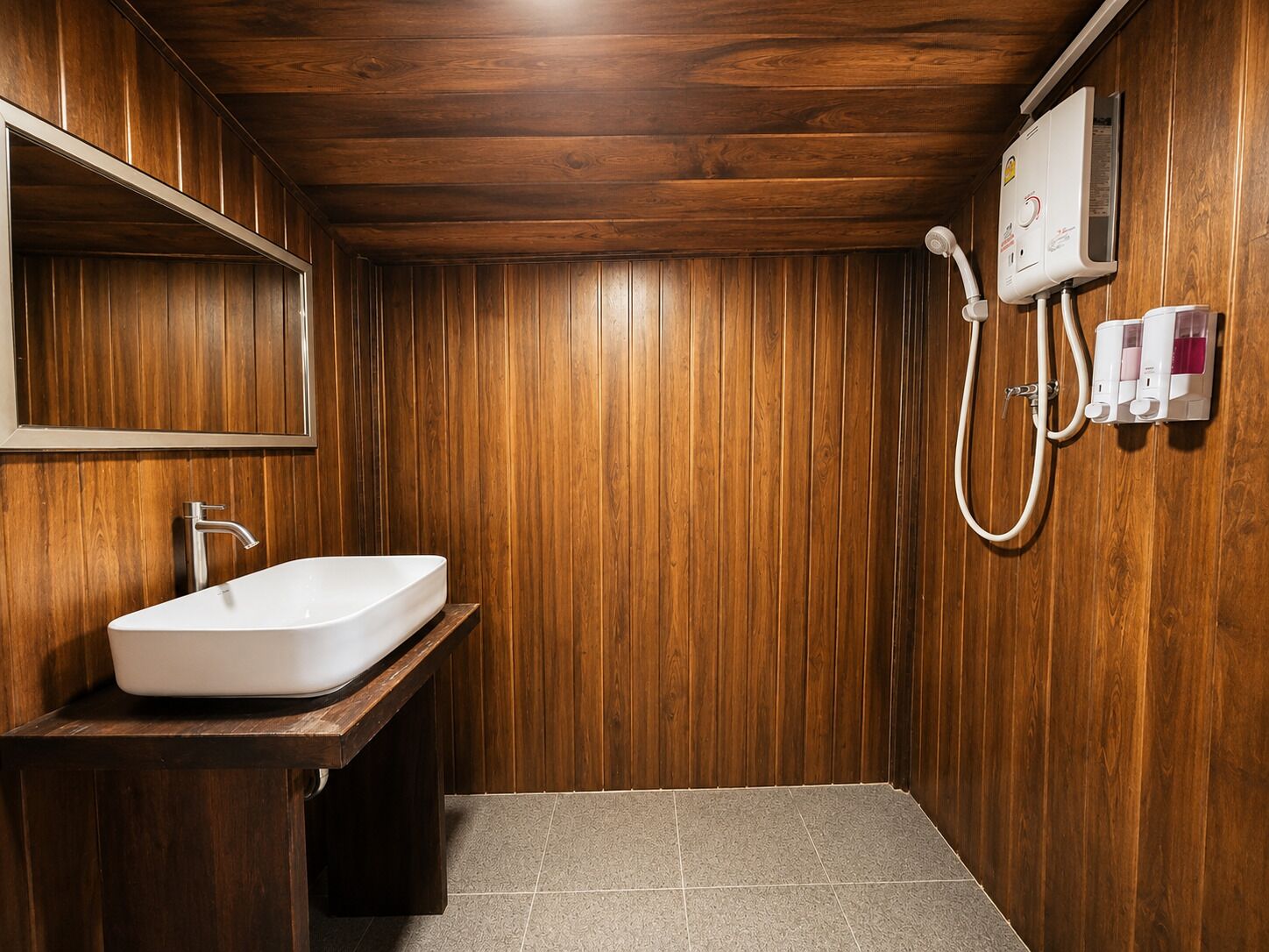 Ein Badezimmer mit Holzvertäfelung, einem weißen Waschbecken, einem Spiegel und einer Duschkabine.