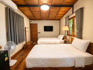 A hotel room with two beds, a TV, a fan, and a window with curtains.