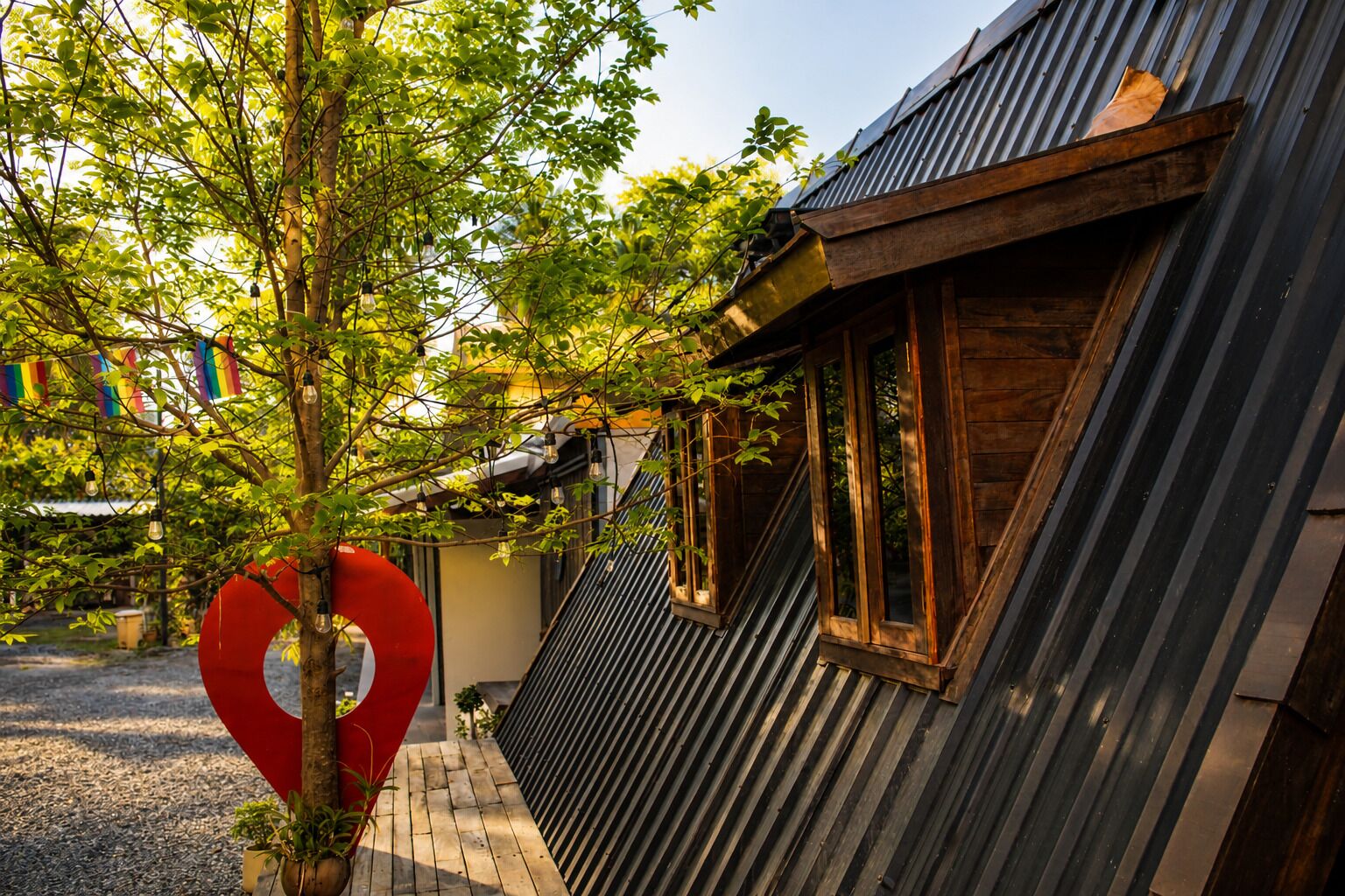 A modern building with a sloped roof, wooden windows, and a red heart-shaped object near a tree.