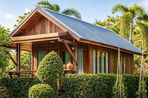 A wooden cabin with a sloped roof, surrounded by dense greenery and palm trees. - Punnattha House by Peema Villa (U Thong)