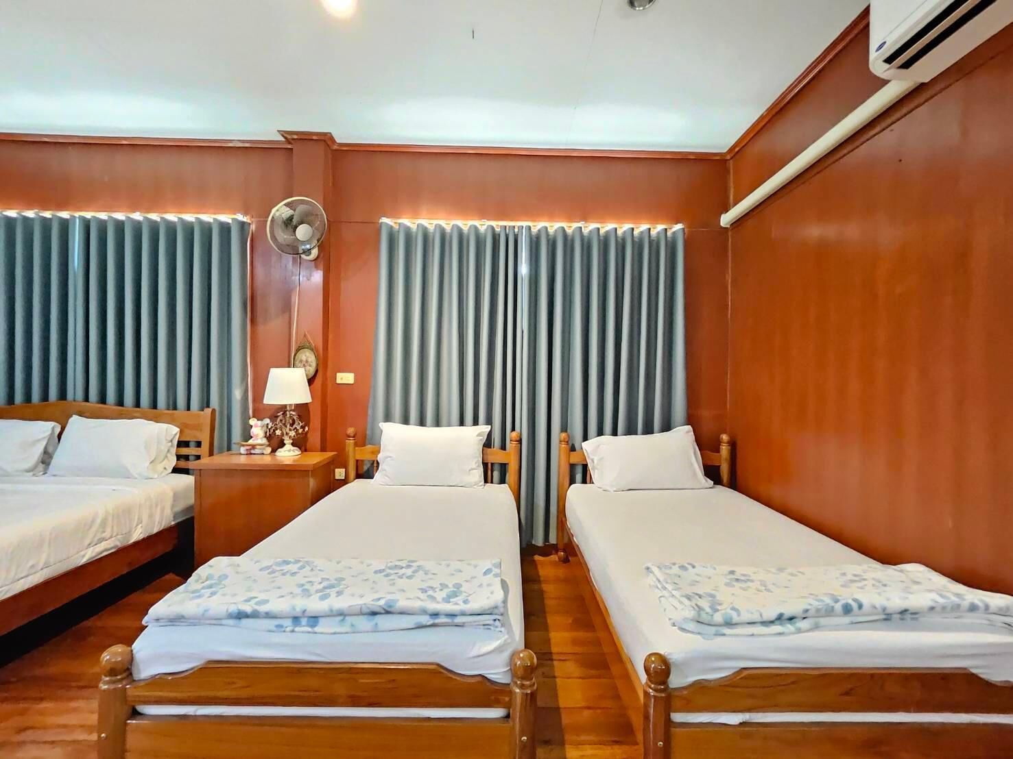 A hotel room with two single beds, a bedside table with a lamp, a wall-mounted air conditioner, and a window with curtains.