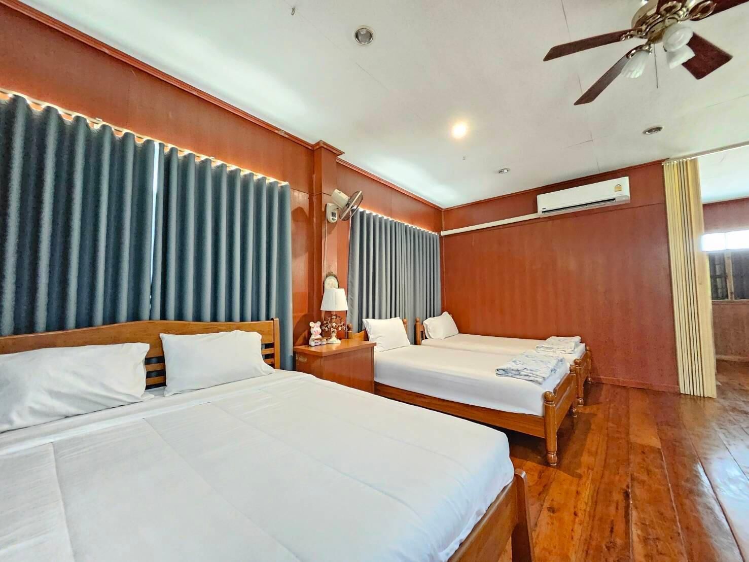 A hotel room with two beds, a ceiling fan, an air conditioning unit, and a window with curtains.