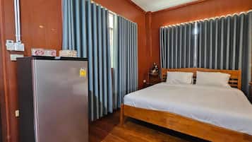 A hotel room with a wooden bed, a refrigerator, and curtains.