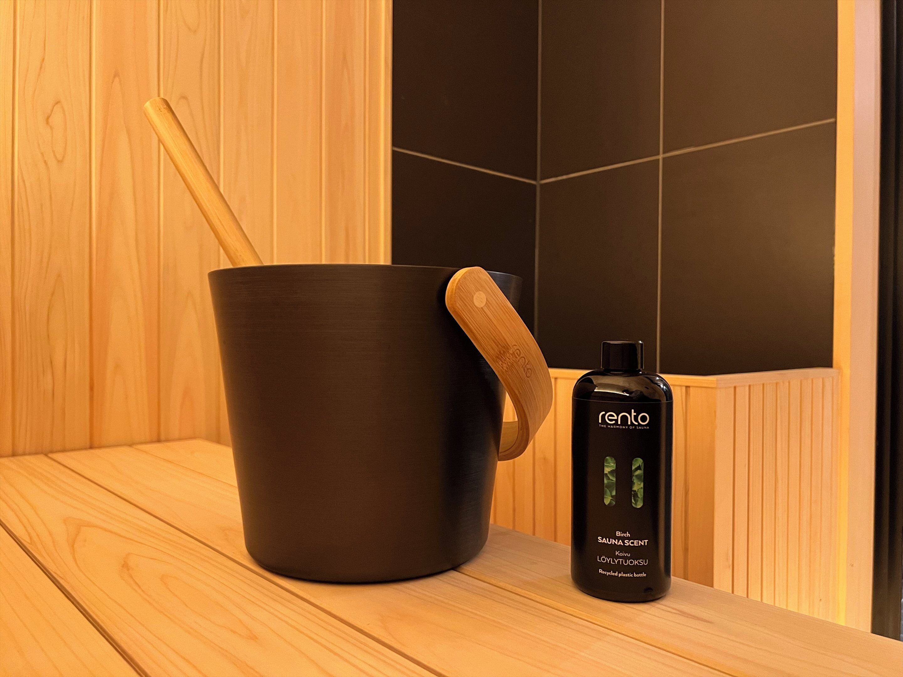 A sauna room with a black bucket and a bottle of Rento sauna scent.