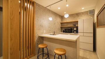 Una cocina moderna con un separador de madera, dos taburetes, un refrigerador, un microondas y un lavamanos.