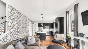 A modern living room with a sofa, a coffee table, and a dining area with a kitchen in the background. - Luxury Rooftop Townhome w/ Skyline Views /Broadway (Nashville)