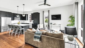 A modern kitchen with dark cabinets, a white countertop, and a dining area with a sofa and chairs. - Luxury Rooftop Townhome w/ Skyline Views /Broadway (Nashville)