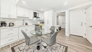 A modern kitchen with white cabinets, a glass dining table, and grey chairs. - 2 bedrooms one bath walk out basement (Calgary)