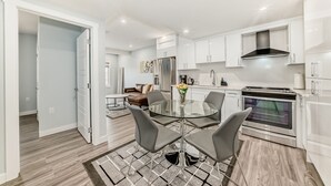 A modern kitchen with white cabinets, a stainless steel oven, and a glass dining table with four chairs. - 2 bedrooms one bath walk out basement (Calgary)