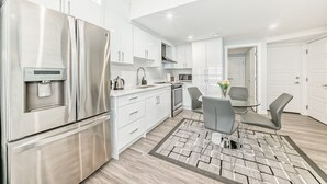 A modern kitchen with stainless steel appliances, white cabinetry, and a dining area with grey chairs. - 2 bedrooms one bath walk out basement (Calgary)