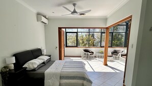 A bedroom with a bed, a nightstand, a lamp, a ceiling fan, and a view of the outdoors through large windows. - Mini Retreat Estuary 
For families (Bouvard)