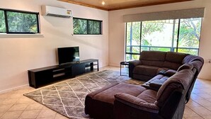 A modern living room with a wooden ceiling, a large window, a brown sofa, a black entertainment unit, and a patterned rug. - Mini Retreat Estuary 
For families (Bouvard)