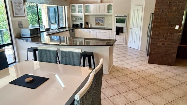 A modern kitchen with a central island, white cabinetry, and a tiled floor. - Mini Retreat Estuary 
For families (Bouvard)