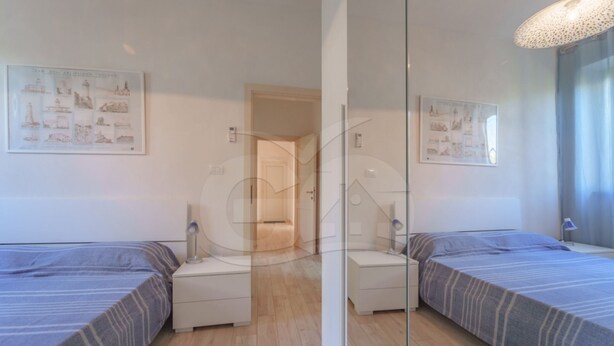 Un dormitorio con dos camas, piso de madera, un armario blanco y una puerta que da a otra habitación.