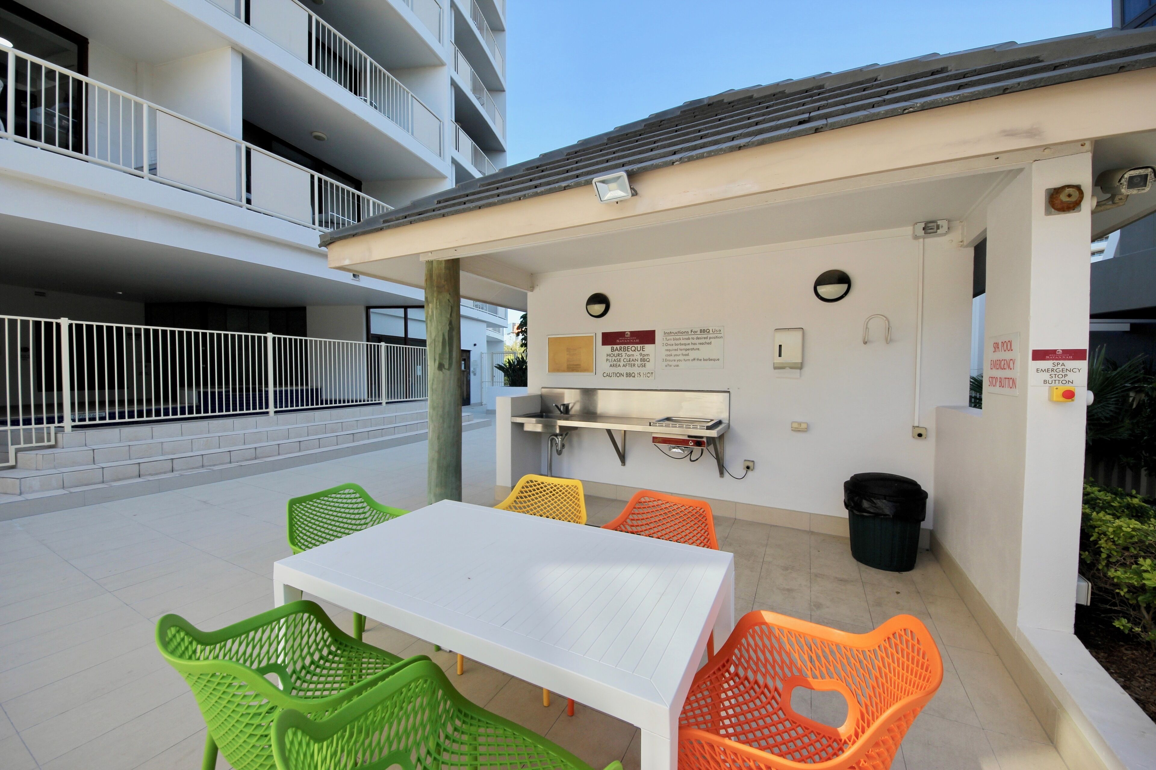 An outdoor patio area with a white table and chairs, a barbecue grill, and a trash can.