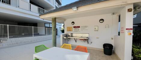 An outdoor patio area with a white table and chairs, a barbecue grill, and a trash can.