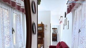 A narrow hallway with a red sofa, lace curtains, and a wooden cabinet. - Maggy's Home - Maggy's Home (2) (Capoliveri)