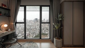 Una habitación moderna con un ventanal amplio, un escritorio con lámpara, una silla, una planta en maceta y un armario.