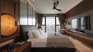 Un dormitorio moderno con una cama grande, ventilador de techo, televisión y vista a la ciudad.