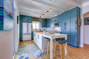 A modern kitchen with teal cabinets, a white island, and bar stools.