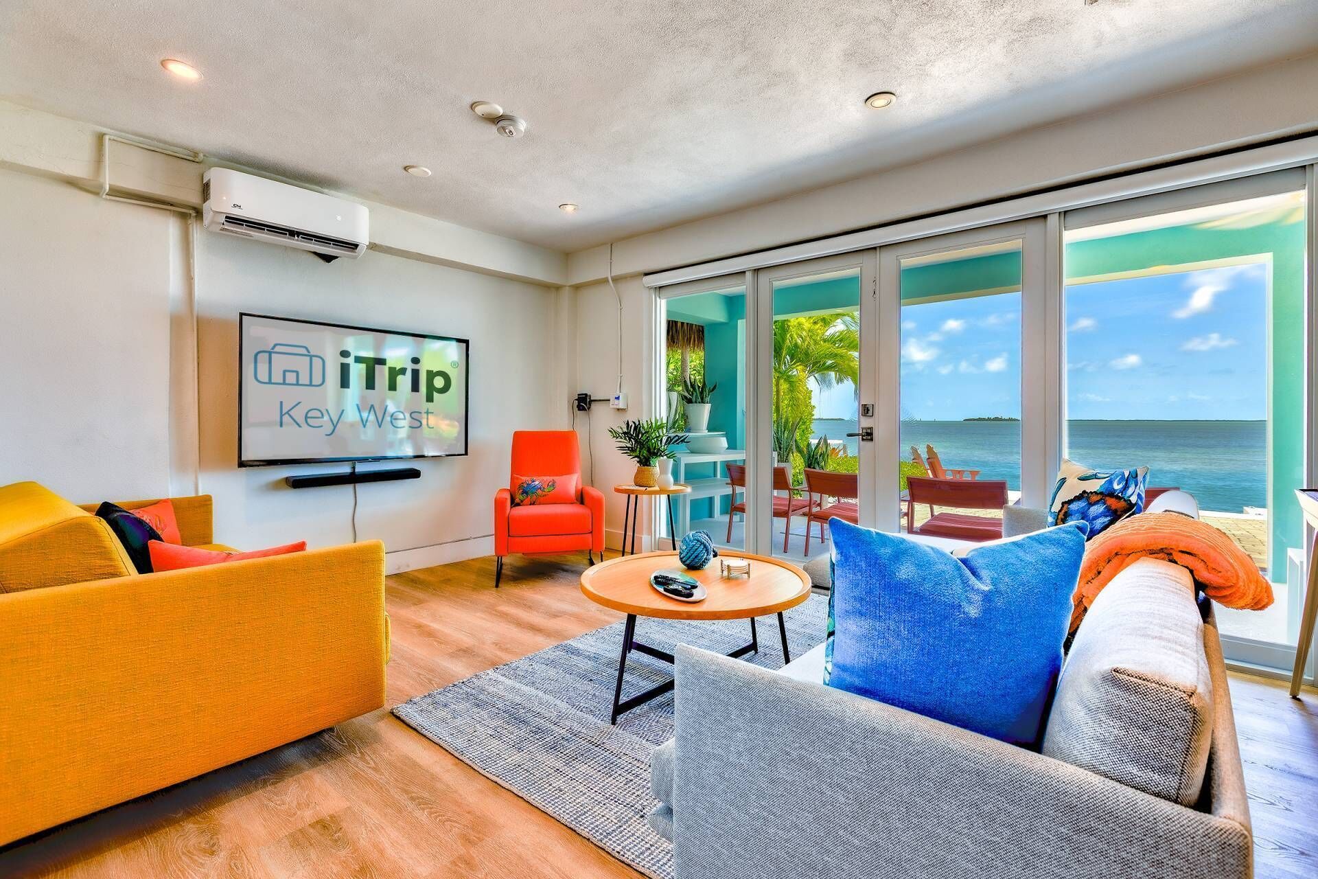 A modern living room with a large TV, comfortable seating, a small table, and a view of the ocean.