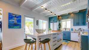A modern kitchen with blue cabinets, a central island, bar stools, and a painting of a sailboat. - Sunset Serenity – Open Water Paradise | Dockage, Sunset Views, Dog Friendly & Minutes to Key West (Summerland Key)