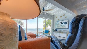 A modern room with a view of the ocean, a ceiling fan, a sign for 'iTrip Key West', and a leather chair. - Sunset Serenity – Open Water Paradise | Dockage, Sunset Views, Dog Friendly & Minutes to Key West (Summerland Key)