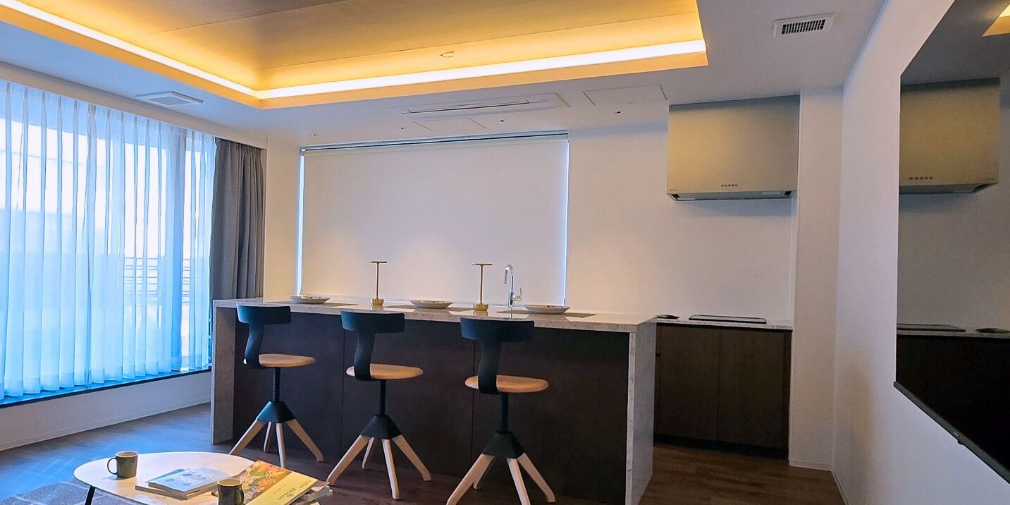 A modern kitchen with a bar area, bar stools, and a large window with curtains.