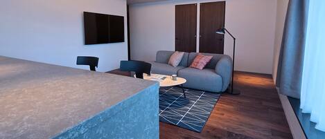 A modern living room with a sofa, coffee table, and a flat-screen TV mounted on the wall.