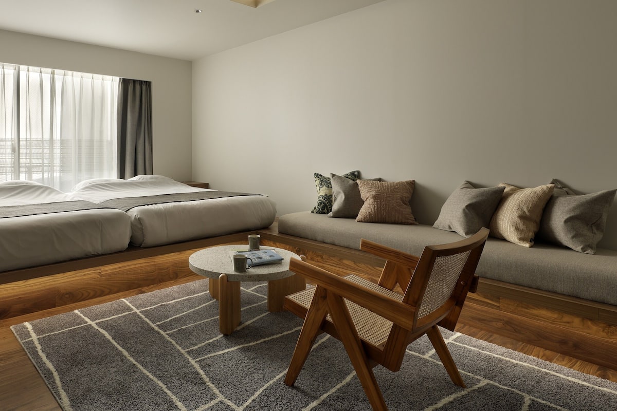 A modern hotel room with a large bed, a sofa, a small round table, and a chair.