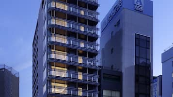 A multi-story building with balconies and a sign indicating it is part of the ACE DENKEN hotel chain.