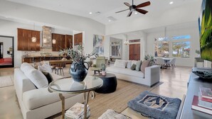 A spacious living area with a sofa, coffee table, and a dining area with chairs. There is a kitchen with wooden cabinets and a stone pillar.
