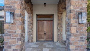 A stone entrance with a double wooden door, a hanging light fixture, and a tiled floor.