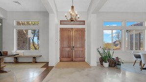 A spacious entryway with a wooden double door, a bench, and potted plants.