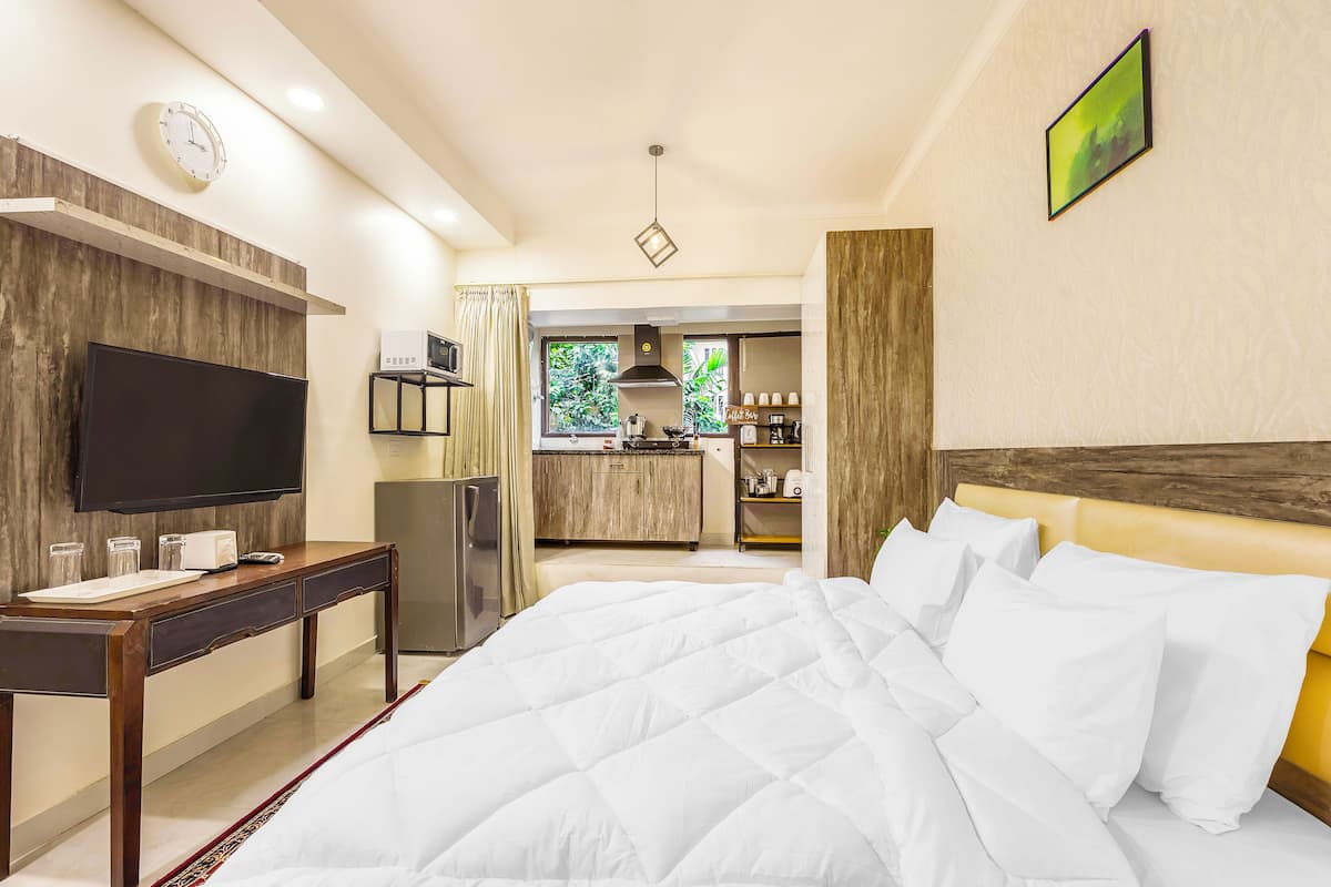 Hotelkamer met een bed, bureau, televisie, keukenhoek en uitzicht op groen.