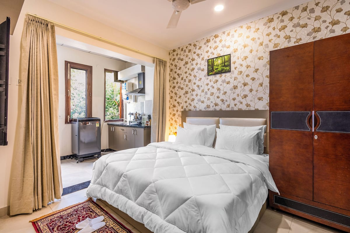Een slaapkamer met een groot bed, een kledingkast, een keukenhoek en een badkamer die door een open deur zichtbaar is.