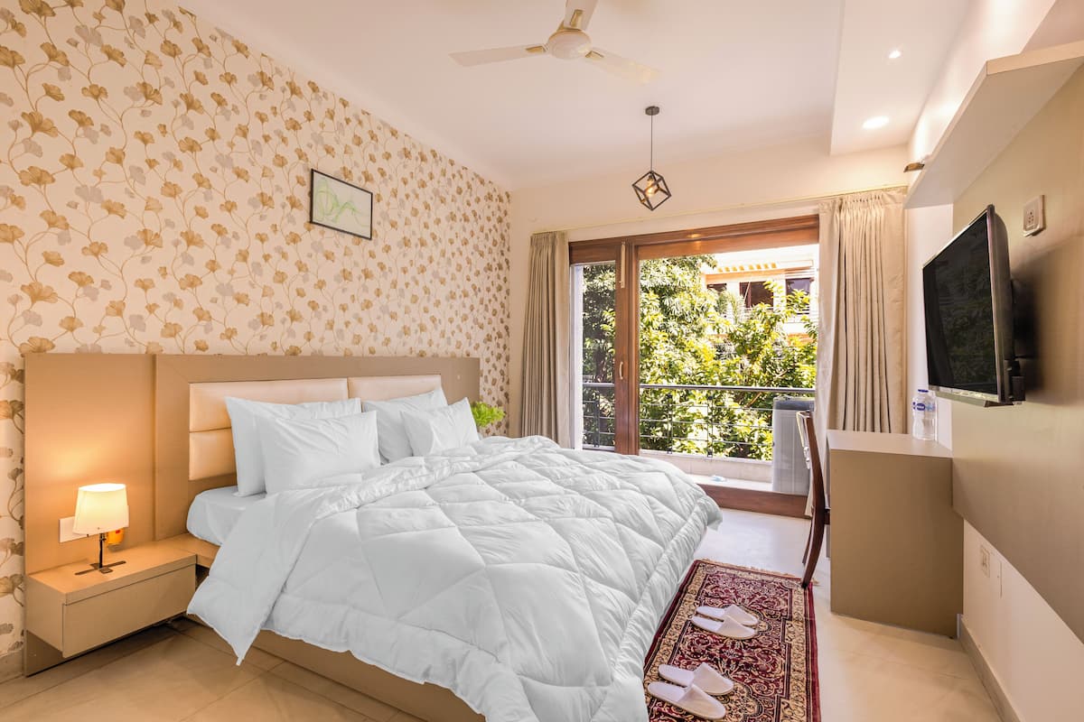 Een hotelkamer met een bed, nachtkastje, televisie en een balkon met uitzicht op groen.
